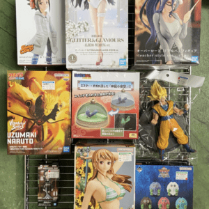 Rack of boxed anime figures on a green surface, featuring Overlord Glitter & Glamours, Naruto, Dragon Ball/DBZ characters, and other figures on a metal grid display.