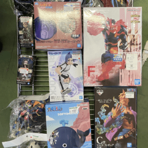 Display rack on a green floor filled with boxed and bagged anime action figures, including Naruto characters and other Bandai models.