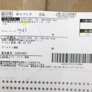 Japanese shipping label on a cardboard box showing sender/recipient details, order number, and a large barcode for tracking.