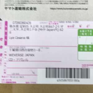 Blurry Japanese shipping label with pink accents and a barcode on a cardboard package; some text is unreadable in the photo.