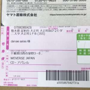 Close-up of a Japanese courier label on a cardboard box, showing a barcode and recipient address fields with pink and green sections.