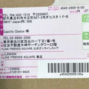 A Japanese shipping label adhered to a cardboard box, showing sender and recipient addresses, magenta stamps, and a black barcode with a tracking code beneath.
