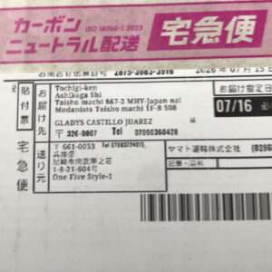 Japanese delivery label on a package showing sender/recipient addresses, a barcode, and the pink '宅急便' logo (Yamato Transport).