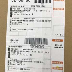Two Japanese shipping labels with black barcodes and printed text on a brown cardboard box, showing tracking numbers, sender/recipient addresses, and 'CD/DVD' item line.