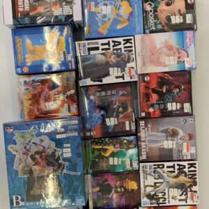 Stack of boxed anime figures on a white table with a black-and-white plush cat on top.