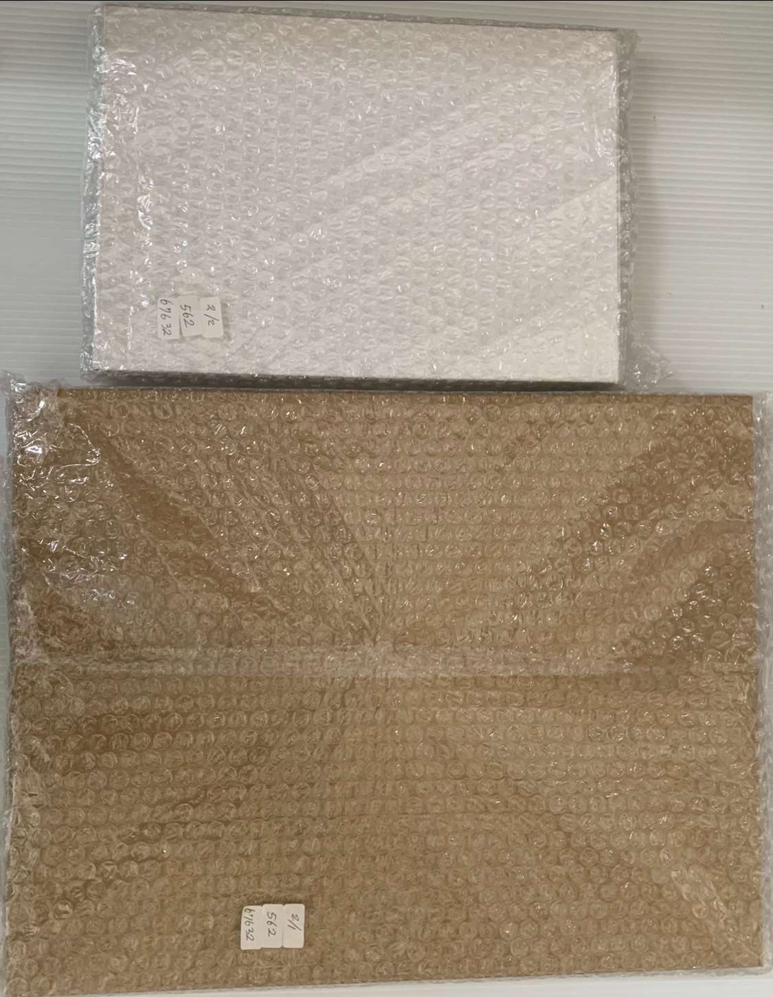 Img_2565 - Articulos Japan (post Box Japan) Two parcels wrapped in bubble wrap, one small white package above a larger brown one, each with small label stickers. Articulos Japan (Post Box Japan)