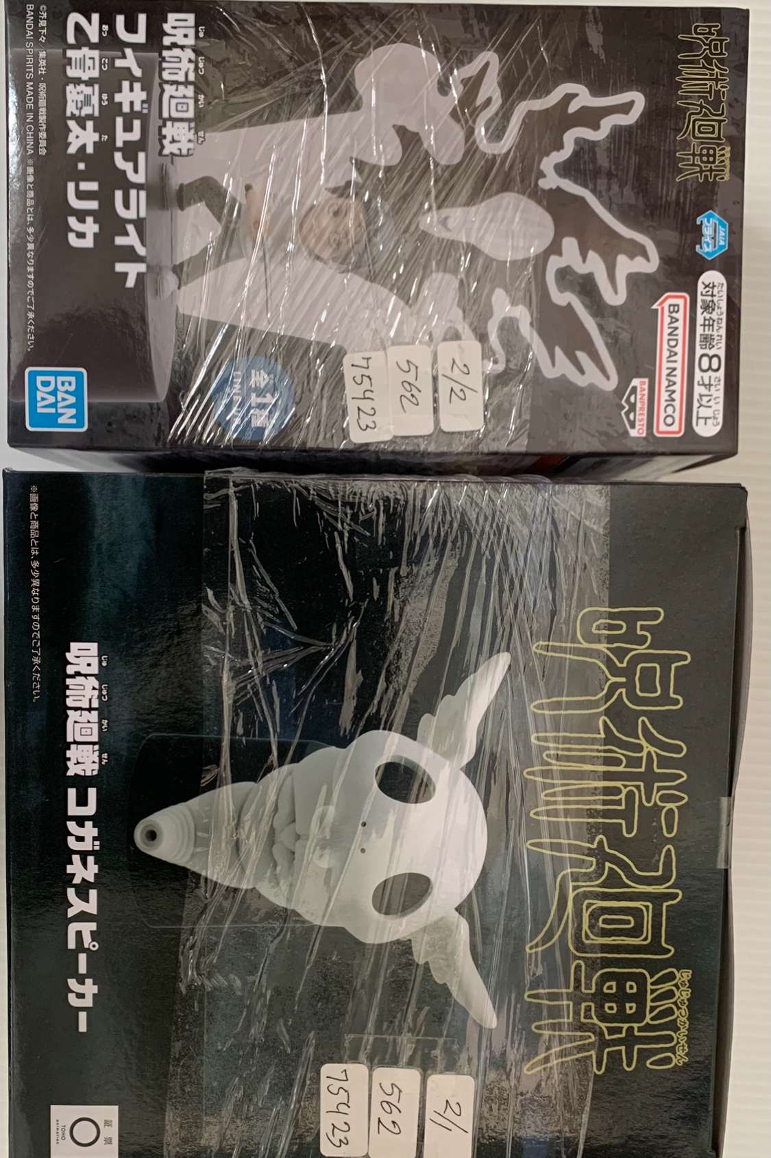 Img_2567 - Articulos Japan (post Box Japan) Two wrapped boxes of Japanese action figures; top box shows a white silhouette and Bandai Namco logos on dark packaging, with Japanese text. Articulos Japan (Post Box Japan)