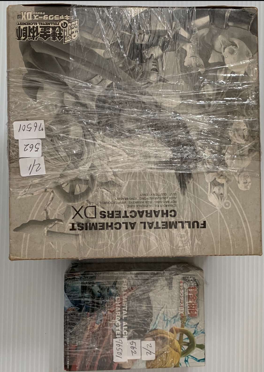 Img_2568 - Articulos Japan (post Box Japan) Two boxed anime action figures on a shelf, the top box labeled 'Fullmetal Alchemist' and wrapped in plastic; a smaller, colorful box sits beneath. Articulos Japan (Post Box Japan)
