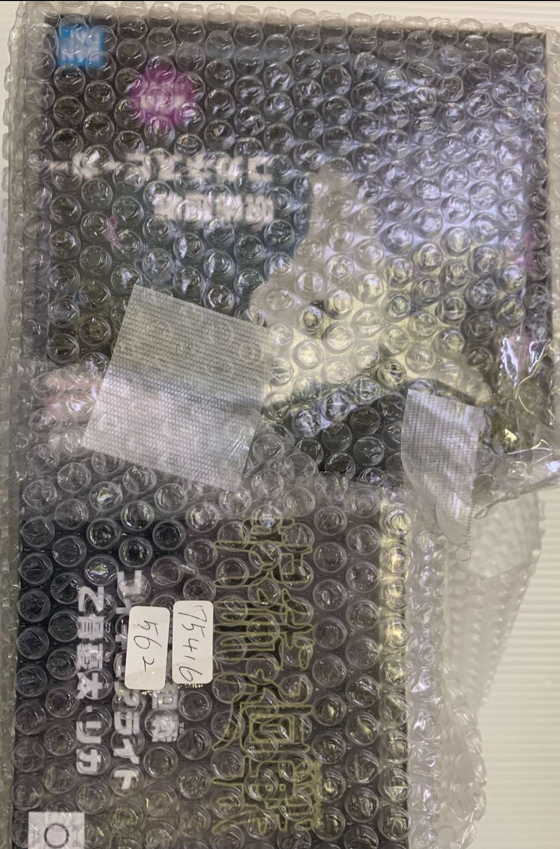 Img_2576 - Articulos Japan (post Box Japan) Bubble-wrapped rectangular package with white label stickers and handwritten numbers; contents not visible through the wrap. Articulos Japan (Post Box Japan)