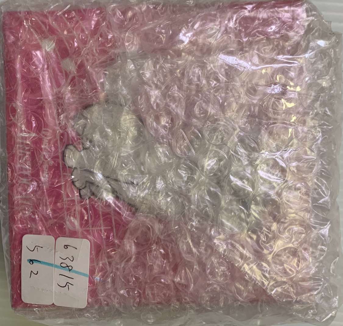 Img_2578 - Articulos Japan (post Box Japan) Pink item wrapped in bubble wrap with two white label stickers in the bottom-left corner, numbers written on them partially visible. Articulos Japan (Post Box Japan)
