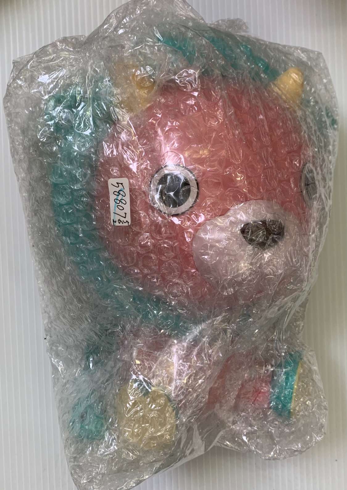 Img_2583 - Articulos Japan (post Box Japan) Pastel unicorn stuffed animal with a pink face, teal mane and ears, and a yellow horn, wrapped in bubble wrap for protection Articulos Japan (Post Box Japan)
