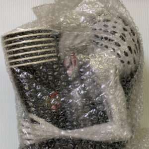 White electronic device tightly wrapped in bubble wrap on a light surface, obscuring details for shipping protection.