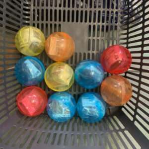 Colorful translucent toy capsules in a gray shopping basket, clustered together on a grid-pattern base.