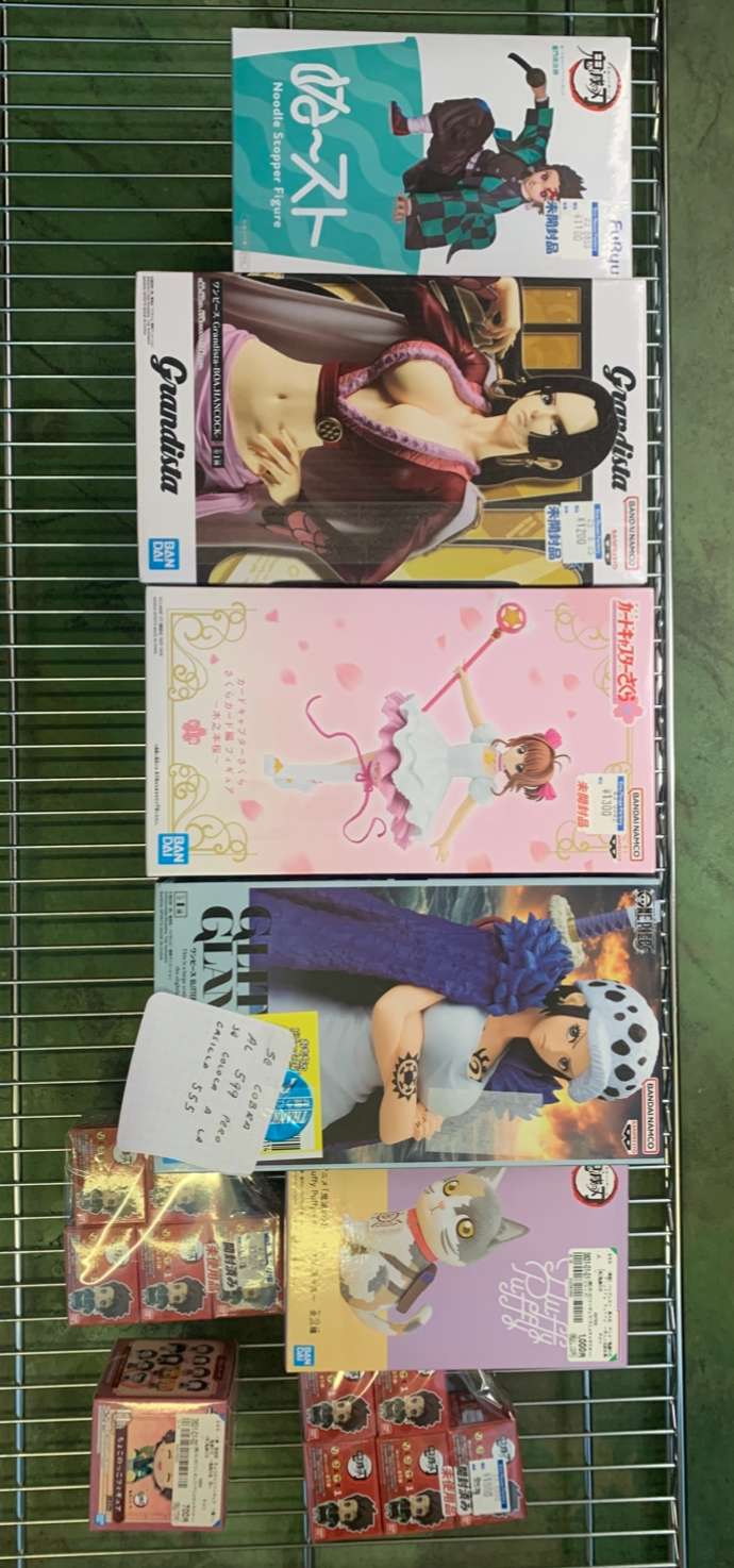 Img_2603 - Articulos Japan (post Box Japan) Shelf of anime figure boxes on a metal rack, varied box art and character designs visible in a store display collection. Articulos Japan (Post Box Japan)