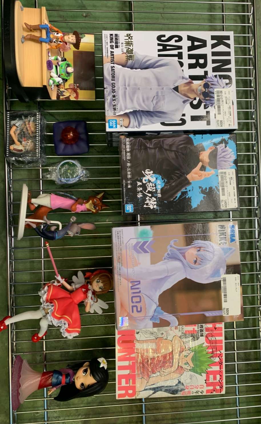 Img_2699 - Articulos Japan (post Box Japan) Wire display rack with anime figurines and Japanese manga magazines, showing colorful character figures around boxed comics. Articulos Japan (Post Box Japan)