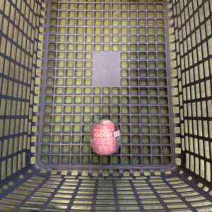 Plastic grid shopping basket with a single pink-wrapped round item at the bottom.