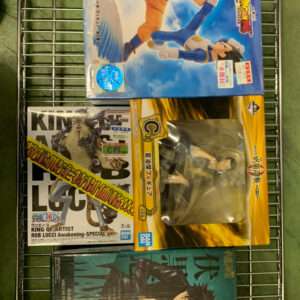 Boxed anime action figures on a metal rack: a Dragon Ball Z figure box on top, a yellow boxed figure in the middle, and a teal/blue box at the bottom.