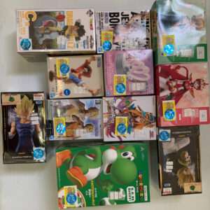 Assorted boxed anime action figures displayed on a light surface, featuring Dragon Ball, One Piece, Mario, and other characters.