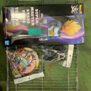 Boxed Dragon Ball Super action figure (Super Saiyan character) on a metal wire shelf, with colorful circular plates in a bag beneath it.