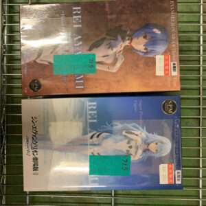 Two boxed anime figures resting on a metal grid rack, one brown box with a blue-haired character above a white-and-blue figure box beneath it, both with green price stickers on the front.