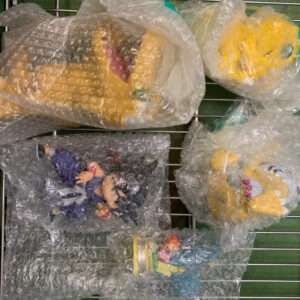 Assorted children's toys and figures wrapped in bubble wrap on a metal wire rack shelf.