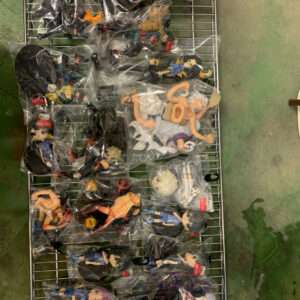 Assorted collectible anime figurines in clear plastic bags laid out on a metal wire shelving rack.