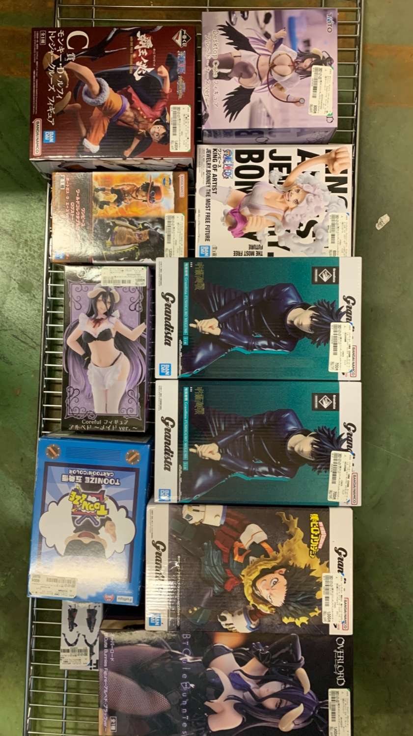 Img_2947 - Articulos Japan (post Box Japan) Assorted boxed anime figures on a metal rack, arranged in two columns, featuring colorful packaging and character art. Row of collectible figure boxes on a store shelf, showing various anime characters in dynamic poses from different brands. A selection of boxed figure sets on a wire display rack, including action-figure boxes with illustrated characters. Boxed anime figurines on a shelving unit, stacked and ready for sale, with vibrant cover art and price stickers. Various character figure boxes on a metal rack, showcasing different anime styles and packaging designs. Articulos Japan (Post Box Japan)