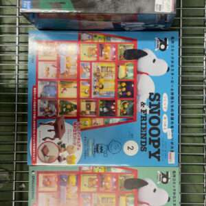 Three Snoopy & Friends books with colorful covers stacked in a metal shopping cart; top book has a black-and-white photo illustration.