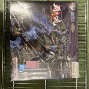 Boxed model figure sealed in plastic on a metal shelf; dark cover features a blue dragon-like creature and Bandai logos.