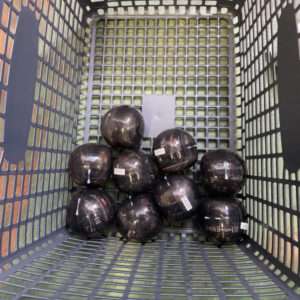 Top-down view of a gray plastic basket filled with dark glossy spheres labeled with small white stickers.