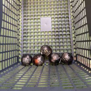 Six black bowling balls resting at the bottom of a blue plastic grid basket.