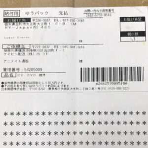 Shipping label on a brown cardboard package with a barcode, Japanese text, and delivery information seen on the top section.