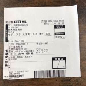 Japanese parcel shipping label showing sender and recipient addresses, phone numbers, and a barcode on a wooden surface.