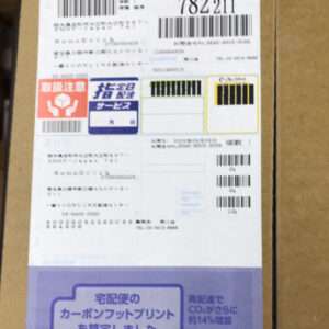 Shipping label on a cardboard box with several barcodes and Japanese text on the label area.