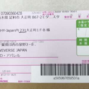 Front of a Japanese shipping label on a brown cardboard box, showing recipient and sender addresses, pink/green service fields, and a barcode.