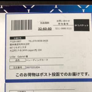 Shipping label on a blue-bordered box with a barcode and Japanese text, showing sender and recipient details.