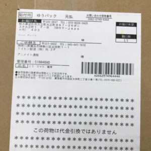 Shipping label on a cardboard box with sender/recipient details, a barcode, and the line 'この荷物は代金引換ではありません' (not COD).