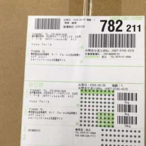 Shipping label on a brown box with multiple barcodes and Japanese text, showing destination details and dates.