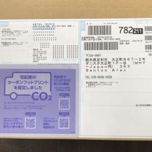 Top view of a cardboard package with multiple shipping labels, barcodes, and a purple CO2 advertisement panel.