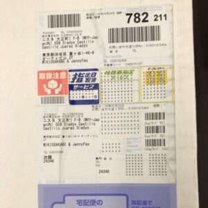 Japanese parcel label with multiple barcodes, stamps, and tracking numbers on a white label.