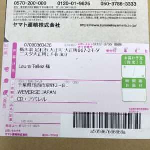 Shipping label on a cardboard box showing recipient Laura Tellez at WEVERSE JAPAN, with a barcode and a green delivery-date box.