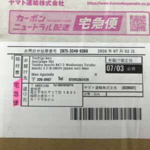 Yamato Transport宅急便の伝票。発送元と宛先の住所、電話番号、デリバリー日07/03が記載された黒文字の用紙。ピンクの付箋で“宅急便”表示が目立つ。