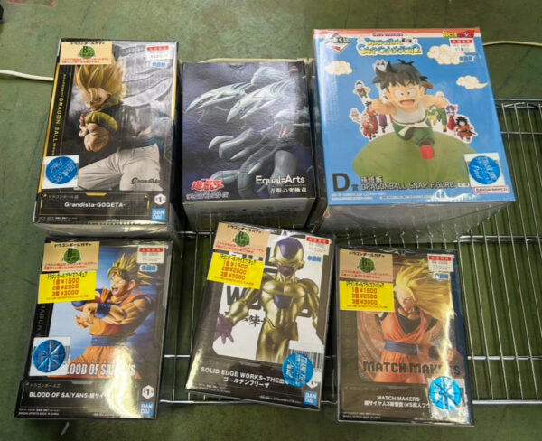 Img_e0675 - Articulos Japan (post Box Japan) Boxed anime figures on a metal display rack; Dragon Ball-themed boxes including Goku and other characters, blue sky-and-clouds box on the right, all unopened. Articulos Japan (Post Box Japan)