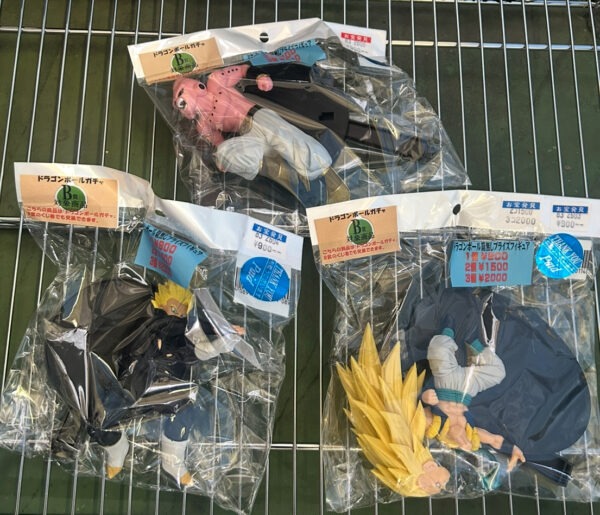 Img_e0695 - Articulos Japan (post Box Japan) Dragon Ball Z action figures in plastic packaging hanging on a metal rack, with characters including a pink figure and a yellow-haired figure visible through the bags. Articulos Japan (Post Box Japan)