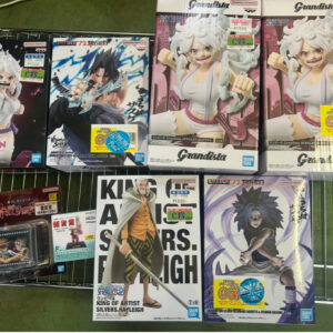 Assortment of anime figure boxes on a metal shelf, featuring Grandista statues of Luffy and other characters with price stickers visible.