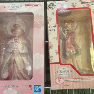 Two boxed collectible figures in decorative packaging on a metal shelf (pink floral box left, floral cream box right).