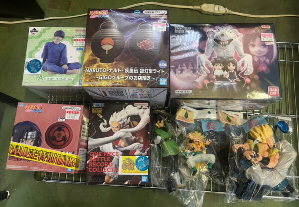 Img_e0720 - Articulos Japan (post Box Japan) Assorted anime figure boxes on a metal rack, including Naruto and One Piece sets, with Dragon Ball figures in plastic packaging nearby. Articulos Japan (Post Box Japan)