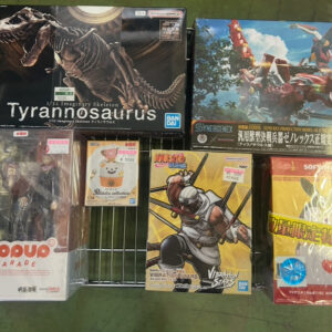 Display of Japanese figure boxes on a wire rack: Tyrannosaurus skeleton figure, a blue transformer-style box, and anime figurines including Yuji Itadori (Pop Up Parade) and Naruto Vibration Stars set, with a yellow boxed item on the right.