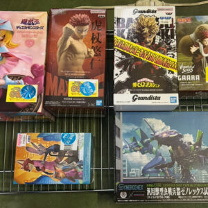 Boxes of anime figure collectibles on a metal rack, featuring characters from Naruto, One Piece, and other series. A display of boxed figurines on a wire shelf, including stylized character figures from popular anime franchises. Set of boxed action figures displayed on a shelf, showing characters in dynamic poses from multiple series. Assorted anime figure boxes on a grid shelf, showcasing collectibles like Grandista and other character figures. Display of large and small boxed figures on a rack, including superhero-style character models from popular anime/manga.]