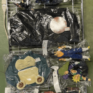 Metal wire display rack with boxed anime figures on the top row and assorted plush toys and character outfits in plastic bags on the lower shelves.
